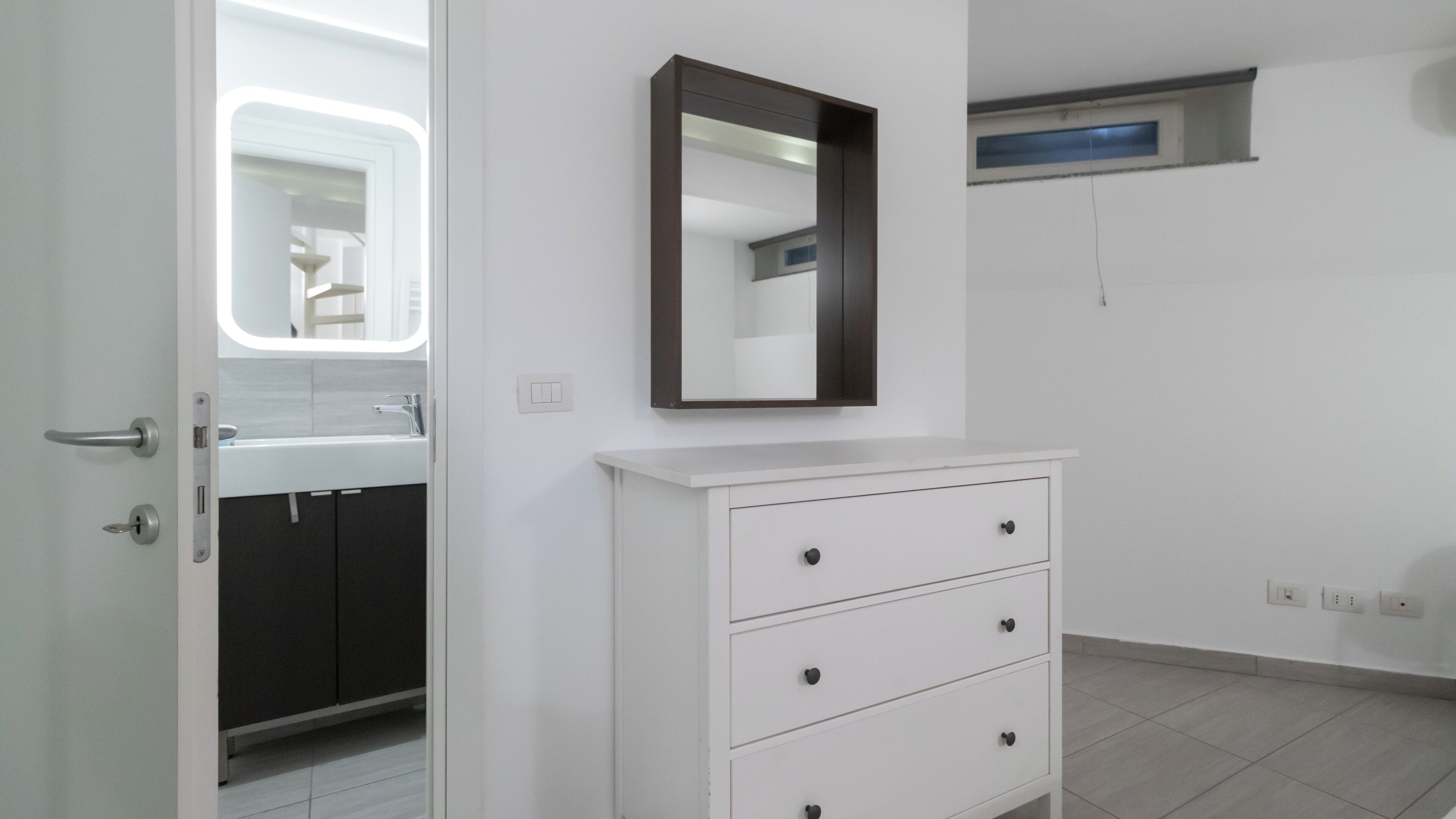 A bathroom with a white vanity, a mirror, and a door leading to a shower area.