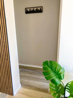 A hallway with a city skyline wall art, wooden flooring, and a large green plant.