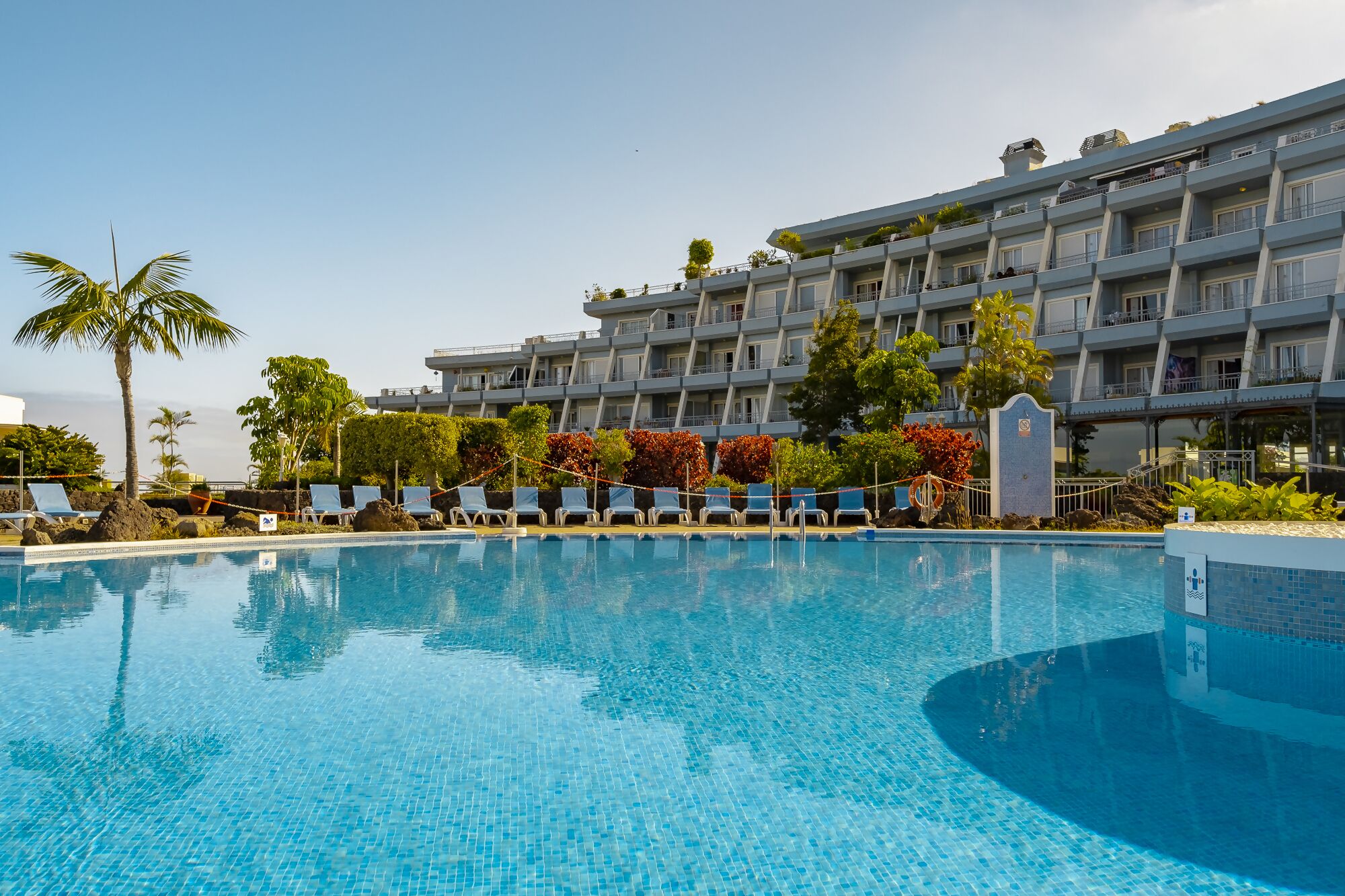 A hotel with a swimming pool, multiple balconies, and lush greenery.