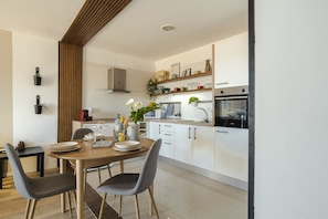 A modern kitchen with white cabinets, a wooden dining table, and two grey chairs.
