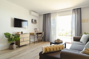 A modern living room with a flat-screen TV, a desk, a sofa, and a large window with curtains.