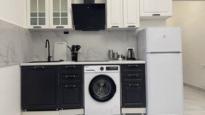Una cocina compacta con lavadora y secadora integradas, armarios blancos y una campana extractora negra.