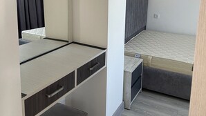 Un dormitorio pequeño con cama, mesita de noche, espejo y un taburete.
