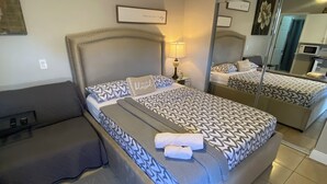 A bedroom with a large bed, a bedside table with a lamp, a bench, and a mirror on the wall. - Luxury, cozy, and Charming studio with WiFi and AC in brilliant Tampa (Tampa)