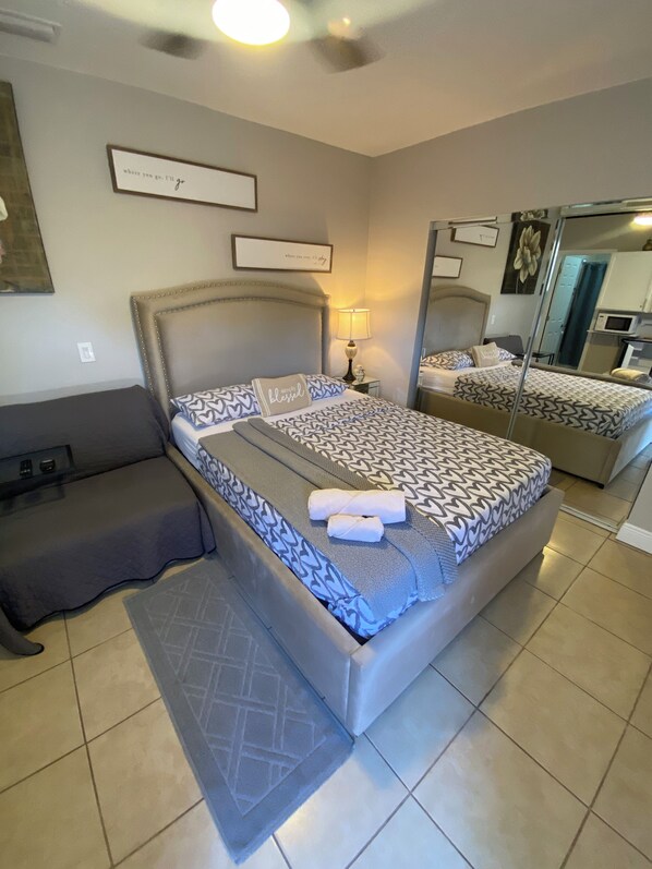 A bedroom with a large bed, a bedside table with a lamp, a bench, and a mirror on the wall.