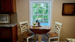 Una cocina con ventana, dos sillas blancas, una mesa de madera y un cuadro en la pared.