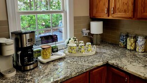Una cocina con cafetera, tarros de té y una ventana con vista a zonas verdes.
