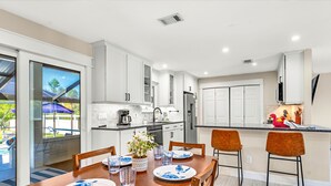 A modern kitchen with white cabinets, a central island, and a dining area with a wooden table and chairs.
