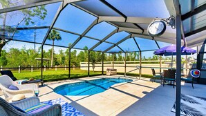 A covered outdoor swimming pool area with lounge chairs, a clock, and a patio umbrella.
