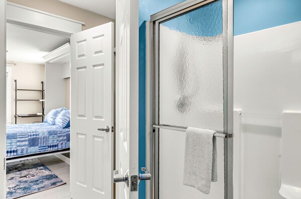 Ein Schlafzimmer mit einem Bett, ein Badezimmer mit Duschabtür aus Glas und ein Flur mit einer weißen Tür.