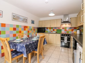 A kitchen with wooden cabinets, a tiled backsplash, and a dining area with a table set for four. - Lobster Pot (Banff)