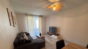 A modern living room with a sectional sofa, a wooden dining table, and a flat-screen TV mounted on a wooden console. - RESIDENCE STEPHANIE (Limoges)