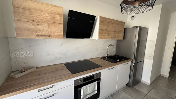 A modern kitchen with wooden cabinets, a black range hood, a stainless steel refrigerator, and a built-in oven. - RESIDENCE STEPHANIE (Limoges)
