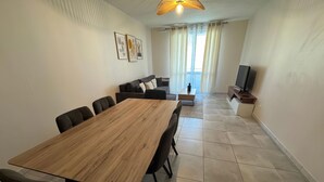 A modern living room with a wooden dining table, black chairs, a sofa, and a TV. - RESIDENCE STEPHANIE (Limoges)