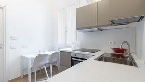 A small, modern kitchen with white cabinetry, a stainless steel sink, and a dining area with two white chairs. - Italianway - Frisi 8 B (Milan)