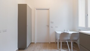 A small, bright room with a white door, a white desk with two chairs, and a window with blinds. - Italianway - Frisi 8 B (Milan)