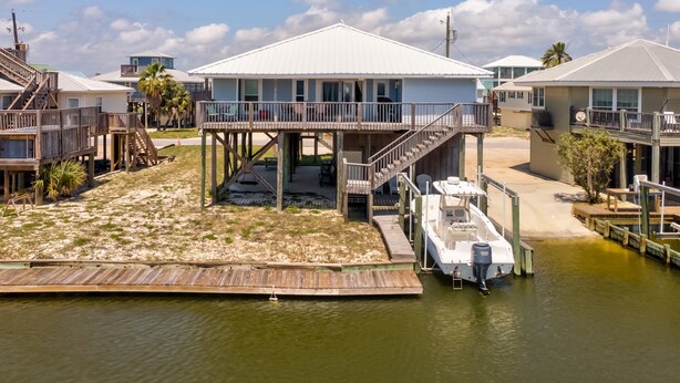 A waterfront property with a house on stilts, a dock, and a boat. - Anchor Eways - 2235 Mallard St 3 Bedroom Home (Dauphin Island)