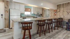 A kitchen with white cabinets, a central island with bar stools, a microwave, and a refrigerator. - Anchor Eways - 2235 Mallard St 3 Bedroom Home (Dauphin Island)