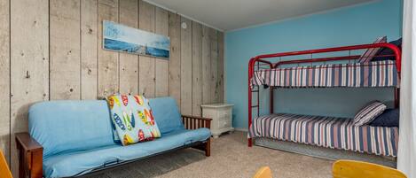 Una habitación con pared de madera, un sofá azul, una cama litera, una mesita y un ventilador de techo.