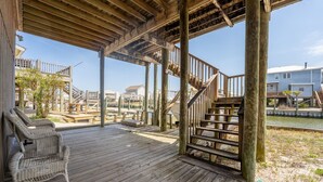 A wooden deck with a wicker chair and a staircase leading to a higher level. - Anchor Eways - 2235 Mallard St 3 Bedroom Home (Dauphin Island)