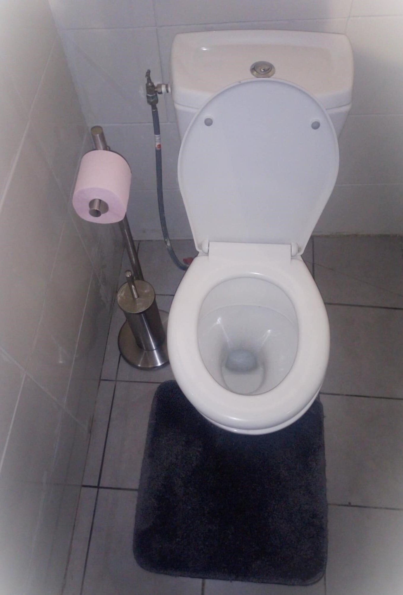 Et badeværelse med et hvidt toilet, en sort badeværelsesmåtte og toiletpapirholder.