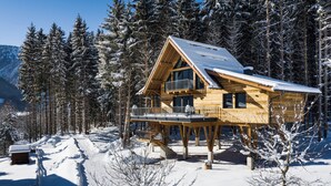 Une cabane en bois dotée d’un balcon, entourée d’arbres couverts de neige et avec une montagne en arrière-plan.