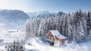 Une cabane en bois entourée d’arbres et de montagnes couverts de neige.