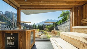 Un espace sauna en bois, doté de bancs et d’un mur de verre offrant une vue sur les montagnes.