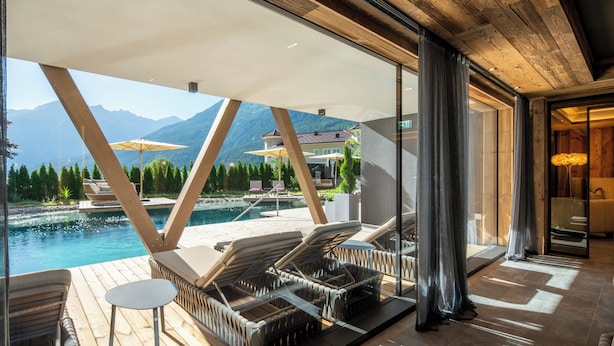 Une chambre d’hôtel moderne dotée d’une grande fenêtre donnant sur une piscine et des montagnes.