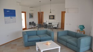 Een woonkamer met twee blauwe banken, een witte salontafel en een eethoek met een tafel en stoelen.