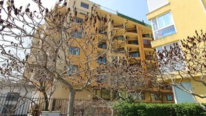 Un edificio de varios pisos con balcones y un árbol en primer plano.