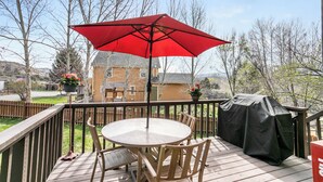 A wooden deck with a round table and chairs, a red umbrella, and a barbecue grill. - 4 Bedroom Remodeled Home with Fenced in Backyard and Garage: Long Term Rental (Gypsum)
