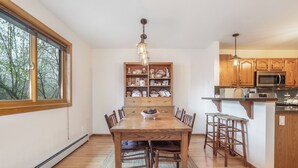 A dining room with a wooden table and chairs, a chandelier, and a kitchen with wooden cabinets and a microwave. - 4 Bedroom Remodeled Home with Fenced in Backyard and Garage: Long Term Rental (Gypsum)