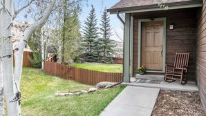 A wooden cabin with a door, a porch with a bench, and a fenced yard with trees. - 4 Bedroom Remodeled Home with Fenced in Backyard and Garage: Long Term Rental (Gypsum)