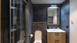 A modern bathroom with a glass shower enclosure, a toilet, a sink with a mirror above, and wooden cabinets. - Apartment in Chantemerle With Family Ski Fun (Saint-Chaffrey)