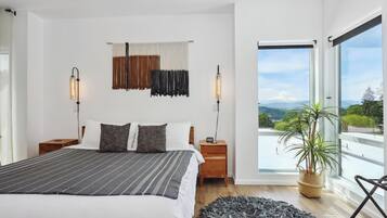 A modern bedroom with a large bed, two bedside tables, a potted plant, and a view of the outdoors.