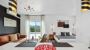 Quarto de hotel moderno com uma janela grande, um sofá de couro marrom, uma mesa de jantar branca e uma tigela decorativa vermelha.