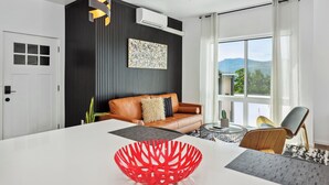 Uma sala de estar moderna com uma mesa de jantar branca, uma tigela decorativa vermelha, um sofá de couro marrom e uma janela grande com vista para o exterior.