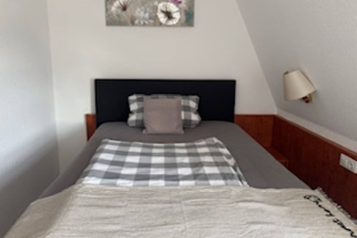 Ein ordentlich eingerichtetes Schlafzimmer mit einem Bett, Kissen, einer karierten Decke und einer Wandlampe.