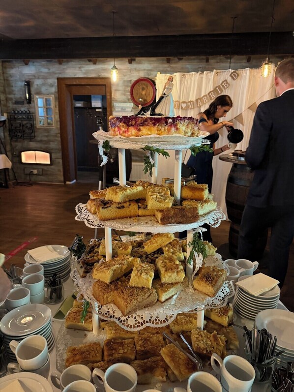 A multi-tiered dessert display at a reception area with a rustic interior, including exposed brick walls and wooden beams.
