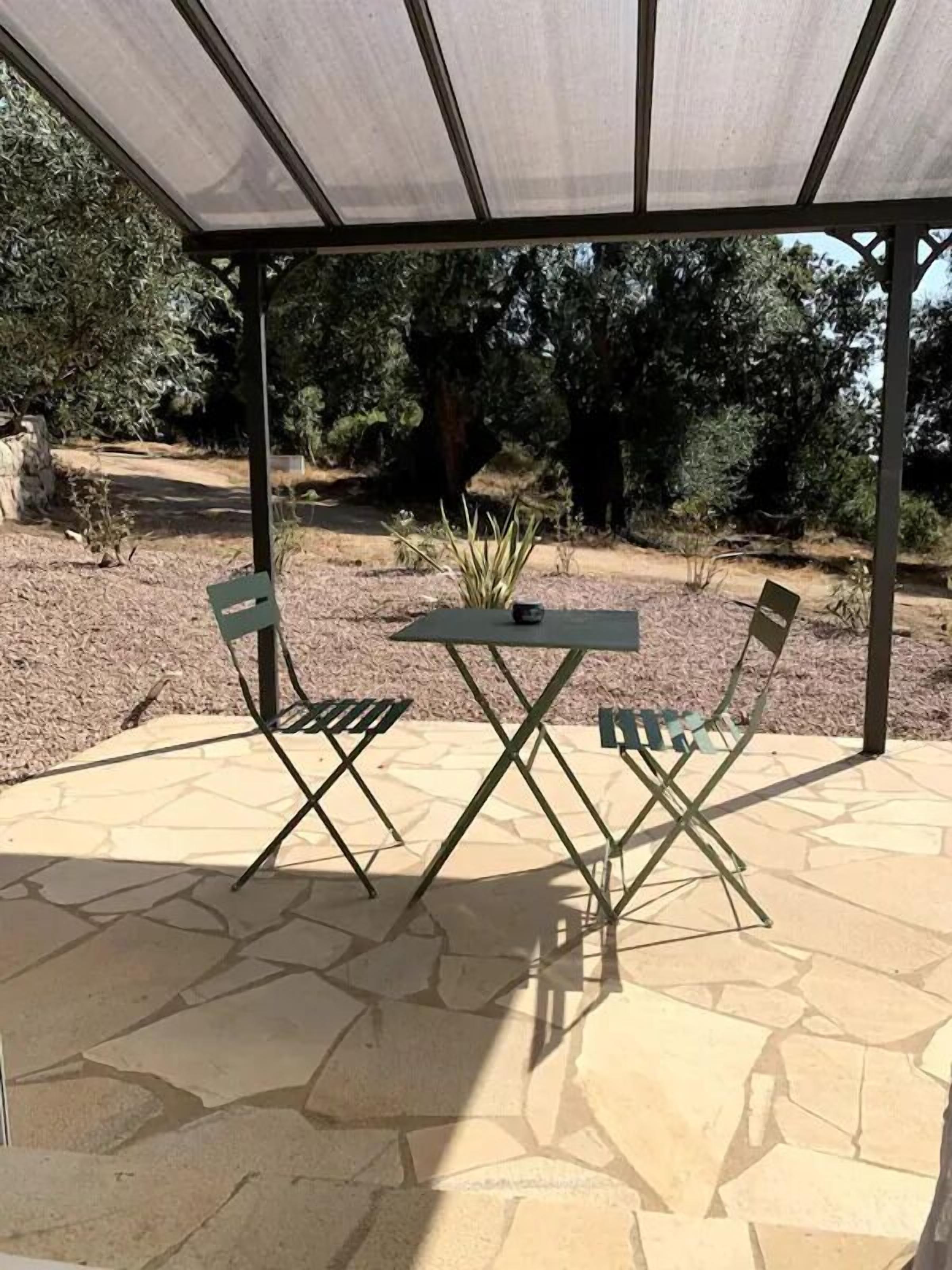An outdoor patio with a covered seating area, stone flooring, and surrounding vegetation.