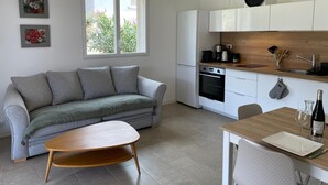 A modern kitchen with white cabinets, a built-in oven, and a wooden countertop. There is a grey sofa with cushions and a wooden coffee table in the living area. - Rsidence Patios di Pruno (Figari)