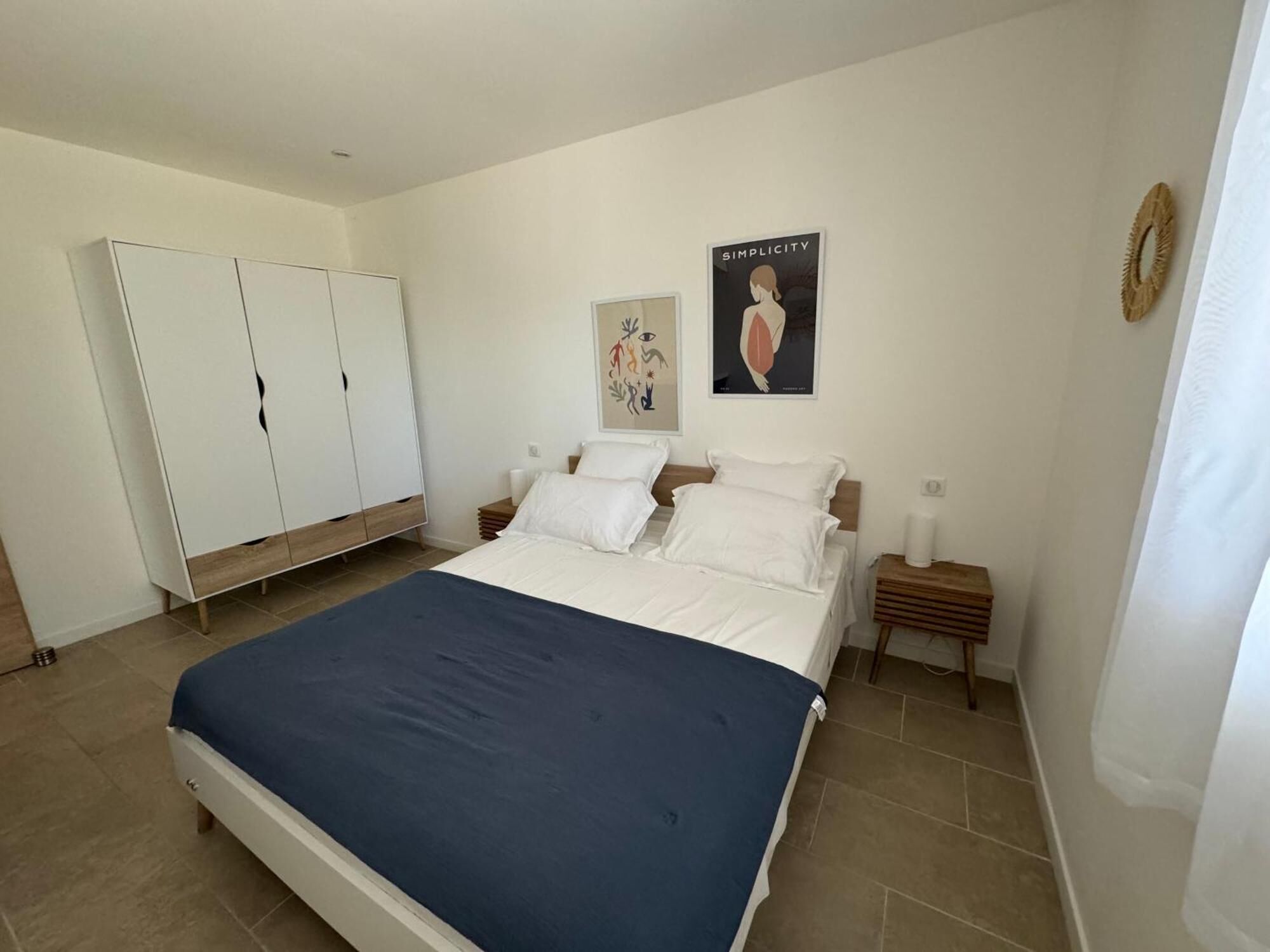 Un dormitorio con una cama, un armario, dos mesitas de noche y dos cuadros decorativos.