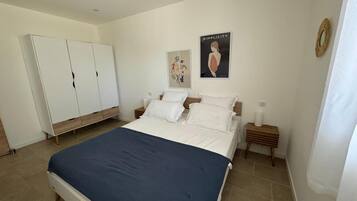 Un dormitorio con una cama, un armario, dos mesitas de noche y dos cuadros decorativos.