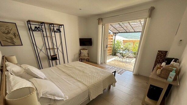 A bedroom with a bed, bedside table, lamp, and a view of the outdoor patio. - Rsidence Patios di Pruno (Figari)