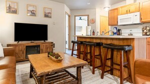 A compact living space with a TV, wooden furniture, a kitchen area, and a dining bar. - Downtown Kalispell Condo Near Glacier & Whitefish (Kalispell)