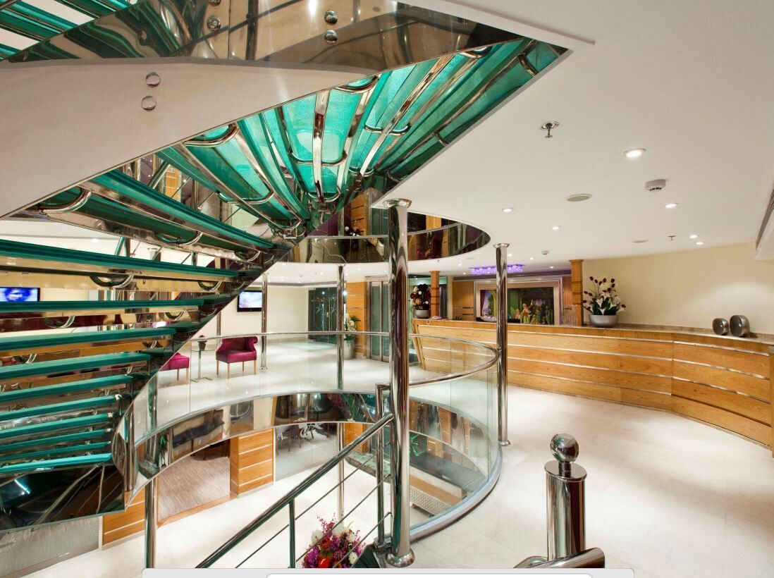 Eine moderne Hotelhalle mit einer gläsernen und metallenen Wendeltreppe, einer Rezeption und einer gebogenen Sitzecke.