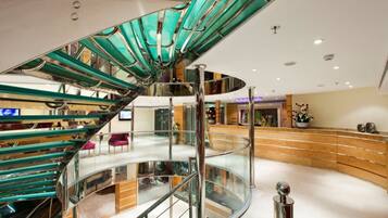 Eine moderne Hotelhalle mit einer gläsernen und metallenen Wendeltreppe, einer Rezeption und einer gebogenen Sitzecke.