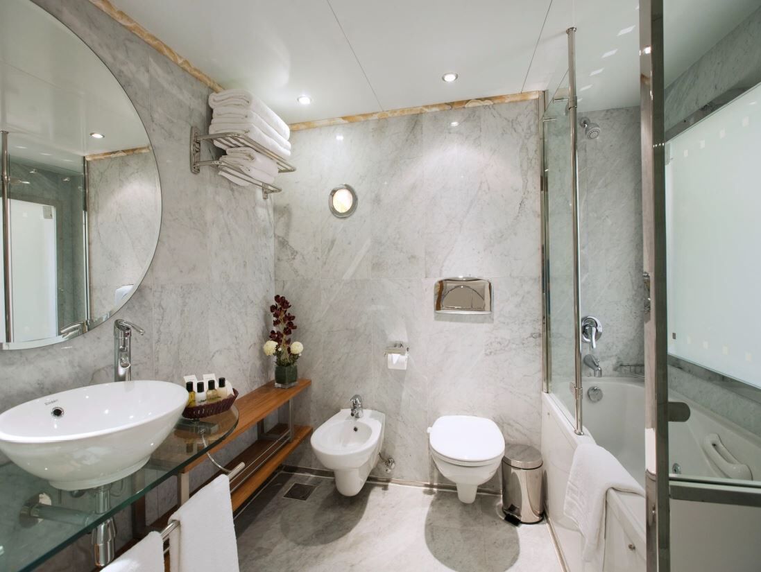 A modern bathroom with a glass sink, bidet, toilet, and a glass-enclosed shower.