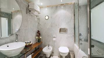 A modern bathroom with a glass sink, bidet, toilet, and a glass-enclosed shower.